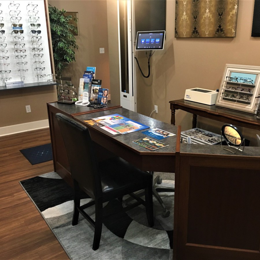 Optical shop interior with a wooden desk, chair, and eyewear display board, warm brown and beige tones